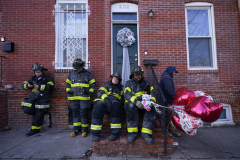 Baltimore City Fire emergency vehicle driver Jamaal Booker, second from right, holds holds balloons given to him by neighbor Darlene Cucina, as a group of fire officials, from left, James Lamartina, Brian Petz, Justin Higley and Chris Hudson stand on a stoop across the street where three firefighters died in a building collapse while battling a two-alarm blaze in a vacant row home , Monday, Jan. 24, 2022, in Baltimore. Lt. Paul Butrim, Lt. Kelsey Sadler and EMT/firefighter Kenny Lacayo died during the blaze.