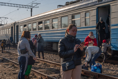Anna Butenko (center right), aged, 26, from Dnipro, reacts as she holds her phone as an evacuation train of Ukrainian refugees from Lviv, Ukraine, to Przemysl, Poland, makes random stop in the Ukrainian countryside. 13 March 2022. Anna was planning to go and stay with her sister in Prague, her father, a firefighter, and boyfriend, in the army, stayed behind. As of January 2023 there are around 8 million Ukrainian refugees outside of the country as the war approaches its one year anniversary.