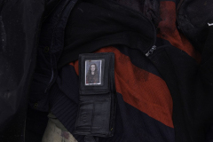 The wallet of a departed man lies upon his blood-soaked shirt displaying the photo of a young girl, presumably his daughter or relative, as he lies in a body bag waiting to be identified and transported to the morgue in Bucha, Ukraine, on 4.6.22. The photo of the young girl is a reminder that the violent departure of one person irreparably alters the lives of countless others, creating an endless network of trauma and loss.