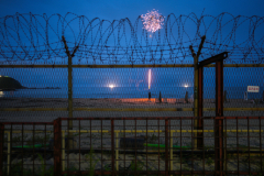 Kim Yul-eun, 12, lights the sky with a firework on Myeongpa Beach, where he is camping with his family in  Goseong-gun, Gangwon-do, South Korea on July 30th, 2022. Myeongpa Beach is the northernmost beach and coastal campsite in South Korea, located just outside the eastern DMZ. ​In recent years, northern counties of South Korea have become unlikely tourist destinations, attracting people drawn to the history of the DMZ. [Project first published July 26, 2023]