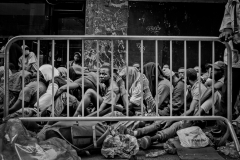 August 1, 2023.  Migrant men line up behind the NYPD metal barricade outside the Roosevelt Hotel in New York City. Migrants are allowed to leave but they stay to keep their place in line, to get food and there was confusion and language barrier. Families get priority for shelter and processing. Men wait outside.  NYC officials have said the city is running out of room to house the migrants, expected to cost the city 12 billion next three years. 600 migrants arrive a day in NYC.