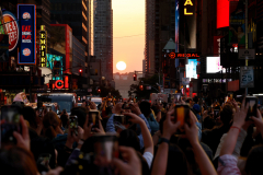 NEW YORK, NY - MAY 30: People stand on 42nd Street in Times Square as they photograph the second evening of Manhattanhenge as the sun, shrouded by smoke from Canadian wildfires sets on May 30, 2023, in New York City.