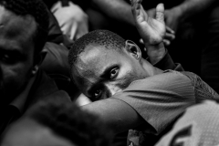August 1, 2023 Migrant men line outside the Roosevelt Hotel in New York City. Migrants are allowed to leave but they stay to keep their place in line, to get food.  There was confusion and a language barrier. Families get priority for shelter and processing. Men wait outside.  NYC officials have said the city is running out of room to house the migrants, expected to cost the city 12 billion next three years.