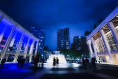 Two people take selfies on a rainy evening at the Lincoln Center fountain.