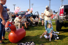 PILESGROVE, NJ USA - AUGUST 24, 2024 -  Lauren Loberto, 3, rests on an inflatable cow she was wrestling with while with her family as they tailgate before the start of the rodeo. They were there celebrating the upcoming nuptials of Sarah and Brenna Roth.