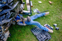 AUGUSTA, NJ USA - AUGUST 5, 2024 -  A pit crew member works on a car’s axle while preparing it for the second night of competition. The second night of the Demolition Derby at the NJ State Fair held at the Sussex County Fairgrounds in Augusta.