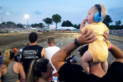 AUGUSTA, NJ USA - AUGUST 4, 2024 - Kyle Stoll, of Branchville, NJ, holds his 8 8-month-old son Beau up as they watch the derby with Chelsea Stoll, Beau’s mother.  The first night of the Demolition Derby at the NJ State Fair held at the Sussex County Fairgrounds in Augusta.