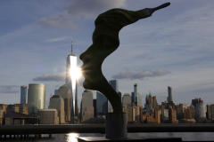 JERSEY CITY, NJ - JANUARY 26: The sun reflects off  the windows of One World Trade Center in New York City behind a sculpture along the Hudson River on January 26, 2025, in Jersey City, New Jersey.