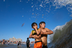 BROOKLYN, NY USA - AUGUST 23, 2025 - A father braces himself while holding his son as the beach is open once again open in Coney Island after Hurricane Erin caused heavy surf the past few days.