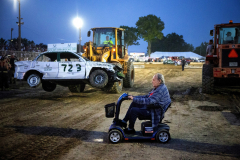 AUGUSTA, NJ, USA - AUGUST 3, 2025 -  A heavy loder pauses, taking a wrecked car out of the arena as an elderly man drives by on his scooter. The first night of the 2025 Demolition Derby during the NJ State Fair held at the Sussex County Fairgrounds.